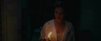 Movie still from “The Mad Women's Ball” (2021), directed by Mélanie Laurent – A woman is holding a lit candle in a dark room; Medium shot, High angle