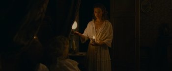 Movie still from “The Mad Women's Ball” (2021), directed by Mélanie Laurent – A woman holding a candle in front of a mirror in the dark; Medium shot, Over the shoulder angle