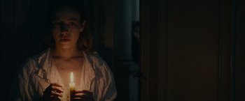 Movie still from “The Mad Women's Ball” (2021), directed by Mélanie Laurent – A woman holding a lit candle in a dark room; Close Up shot, Over the shoulder angle