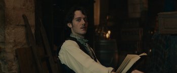 Movie still from “The Mad Women's Ball” (2021), directed by Mélanie Laurent – A man in a vest and tie holding a painting; Close Up shot, Over the shoulder angle