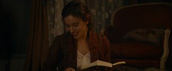 Movie still from “The Mad Women's Ball” (2021), directed by Mélanie Laurent – A woman is smiling while reading a book; Close Up shot, Over the shoulder angle