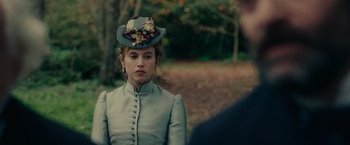 Movie still from “The Mad Women's Ball” (2021), directed by Mélanie Laurent – A woman wearing a hat with flowers on top of her head; Close Up shot, Over the shoulder angle