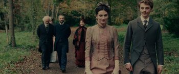Movie still from “The Mad Women's Ball” (2021), directed by Mélanie Laurent – A group of people walking on a dirt path; Medium shot, Over the shoulder angle