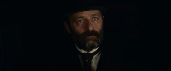 Movie still from “The Mad Women's Ball” (2021), directed by Mélanie Laurent – A man with a beard wearing a suit and a hat; Close Up shot, Low angle