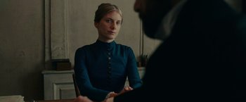 Movie still from “The Mad Women's Ball” (2021), directed by Mélanie Laurent – A woman sitting in front of a man in front of a table; Medium shot, Over the shoulder angle