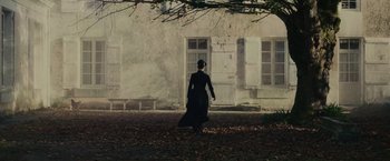 Movie still from “The Mad Women's Ball” (2021), directed by Mélanie Laurent – A woman in a long black dress walking in front of a building; Extreme Wide shot, High angle