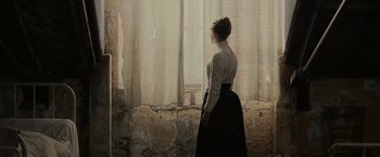 Movie still from “The Mad Women's Ball” (2021), directed by Mélanie Laurent – A woman standing in front of a window looking outside; Medium shot, Over the shoulder angle