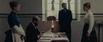 Movie still from “The Mad Women's Ball” (2021), directed by Mélanie Laurent – Two men standing at a table in front of a candle; Medium shot, Low angle