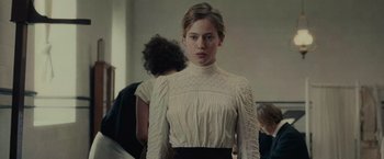 Movie still from “The Mad Women's Ball” (2021), directed by Mélanie Laurent – A woman in a white blouse standing in front of a mirror; Medium shot, Low angle