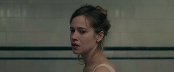 Movie still from “The Mad Women's Ball” (2021), directed by Mélanie Laurent – A woman with a messy bun is looking at the camera; Close Up shot, Over the shoulder angle