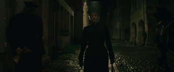 Movie still from “The Mad Women's Ball” (2021), directed by Mélanie Laurent – A woman in a black dress walking down a dark street; Medium shot, Low angle