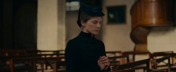 Movie still from “The Mad Women's Ball” (2021), directed by Mélanie Laurent – A woman in a black dress and a hat is praying; Medium shot, Low angle