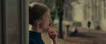 Movie still from “The Mad Women's Ball” (2021), directed by Mélanie Laurent – A woman smoking a cigarette in a park; Close Up shot, Over the shoulder angle
