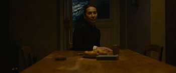 Movie still from “The Mad Women's Ball” (2021), directed by Mélanie Laurent – A person sitting at a table with a plate of food in front of them; Medium shot, High angle