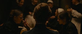 Movie still from “The Mad Women's Ball” (2021), directed by Mélanie Laurent – A group of people sitting in a room; Close Up shot, Over the shoulder angle