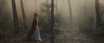 Movie still from “The Mad Women's Ball” (2021), directed by Mélanie Laurent – A woman walking through the woods wearing a long red coat; Wide shot, Low angle