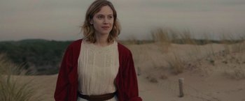 Movie still from “The Mad Women's Ball” (2021), directed by Mélanie Laurent – A woman standing in the sand wearing a white dress and a red jacket; Close Up shot, Over the shoulder angle