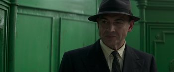 Movie still from “The Man from U.N.C.L.E.” (2015), directed by Guy Ritchie – A man in a suit and hat standing in front of a green door; Close Up shot, Over the shoulder angle