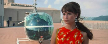 Movie still from “The Man from U.N.C.L.E.” (2015), directed by Guy Ritchie – A woman in an orange and yellow dress standing next to a helicopter; Medium shot, Low angle