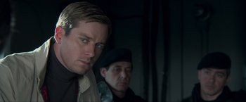 Movie still from “The Man from U.N.C.L.E.” (2015), directed by Guy Ritchie – A man standing next to another man in a room; Close Up shot, Over the shoulder angle