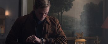Movie still from “The Man from U.N.C.L.E.” (2015), directed by Guy Ritchie – A young man looking at his watch while wearing a brown jacket; Medium shot, Low angle