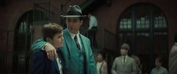 Movie still from “The Many Saints of Newark” (2021), directed by Alan Taylor – A man in a suit and a hat standing next to a young boy; Medium shot, Over the shoulder angle