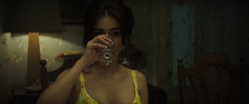 Movie still from “The Many Saints of Newark” (2021), directed by Alan Taylor – A woman in a yellow dress drinking a glass of water; Close Up shot, Over the shoulder angle