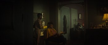 Movie still from “The Many Saints of Newark” (2021), directed by Alan Taylor – A woman sitting in a chair in a living room; Medium shot, Over the shoulder angle