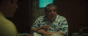 Movie still from “The Many Saints of Newark” (2021), directed by Alan Taylor – An older man sitting at a table in front of a plate of food; Medium shot, Low angle