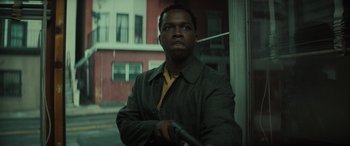 Movie still from “The Many Saints of Newark” (2021), directed by Alan Taylor – A man holding a gun in front of a building; Close Up shot, Low angle