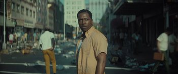 Movie still from “The Many Saints of Newark” (2021), directed by Alan Taylor – A man standing on the side of the road in a city; Medium shot, Low angle