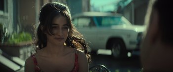 Movie still from “The Many Saints of Newark” (2021), directed by Alan Taylor – A beautiful young lady sitting in front of a car on the side of the road; Close Up shot, Over the shoulder angle