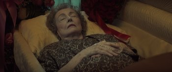 Movie still from “The Many Saints of Newark” (2021), directed by Alan Taylor – An older woman laying on a bed with pearls on it; Medium shot, High angle