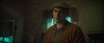 Movie still from “The Many Saints of Newark” (2021), directed by Alan Taylor – A man wearing glasses and a hat standing in front of a window; Close Up shot, Low angle