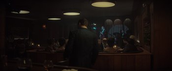Movie still from “The Many Saints of Newark” (2021), directed by Alan Taylor – A man standing in front of a group of people in a room; Wide shot, Over the shoulder angle