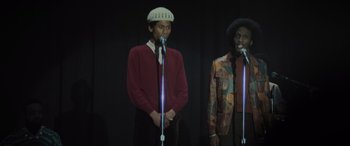 Movie still from “The Many Saints of Newark” (2021), directed by Alan Taylor – Two men stand on a stage with microphones; Medium shot, Low angle