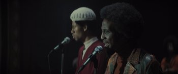 Movie still from “The Many Saints of Newark” (2021), directed by Alan Taylor – A couple of men standing next to each other on microphones; Close Up shot, Low angle