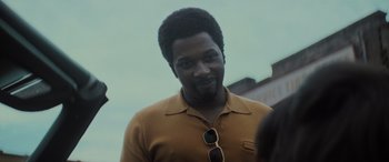 Movie still from “The Many Saints of Newark” (2021), directed by Alan Taylor – A person wearing sunglasses and a polo shirt; Close Up shot, Over the shoulder angle