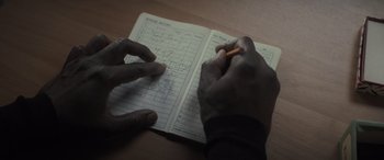Movie still from “The Many Saints of Newark” (2021), directed by Alan Taylor – A person is writing in a notebook on a table; Extreme Close Up shot, High angle