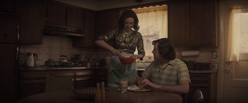 Movie still from “The Many Saints of Newark” (2021), directed by Alan Taylor – Two people sitting at a table in a kitchen preparing food; Medium shot, Over the shoulder angle