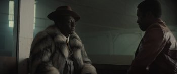 Movie still from “The Many Saints of Newark” (2021), directed by Alan Taylor – A man in a fur coat and hat sitting in a chair; Medium shot, Low angle