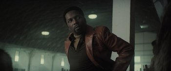 Movie still from “The Many Saints of Newark” (2021), directed by Alan Taylor – A man wearing a brown jacket standing in a room; Medium shot, Low angle