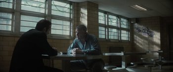 Movie still from “The Many Saints of Newark” (2021), directed by Alan Taylor – An older man sitting at a table in a jail cell; Medium shot, Over the shoulder angle