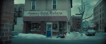 Movie still from “The Many Saints of Newark” (2021), directed by Alan Taylor – A person laying on the ground in front of a bakery; Extreme Wide shot, High angle
