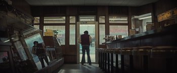 Movie still from “The Many Saints of Newark” (2021), directed by Alan Taylor – A man standing in front of a window in a restaurant; Wide shot, Low angle