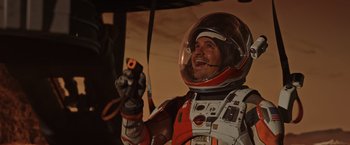 Movie still from “The Martian” (2015), directed by Ridley Scott – A man in a spacesuit holding a remote control; Medium shot, Overhead angle