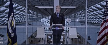 Movie still from “The Martian” (2015), directed by Ridley Scott – A man in a suit and tie standing in front of a podium; Wide shot, Low angle