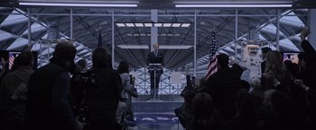 Movie still from “The Martian” (2015), directed by Ridley Scott – A man is speaking at an event in front of a group of onlookers; Wide shot, Over the shoulder angle