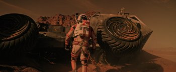 Movie still from “The Martian” (2015), directed by Ridley Scott – A man standing next to an off - road vehicle; Wide shot, High angle