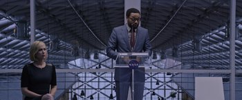 Movie still from “The Martian” (2015), directed by Ridley Scott – A man standing at a podium in front of a building; Medium shot, Low angle